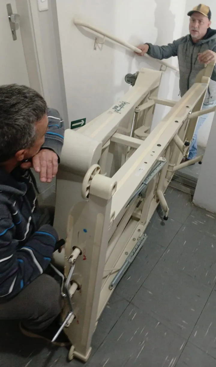 Flávio e Rogério transportam cama hospitalar pelas escadas